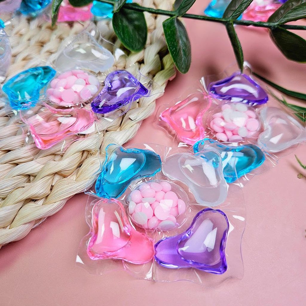 Colorful heart-shaped capsules on a pink surface with green leaves in the background